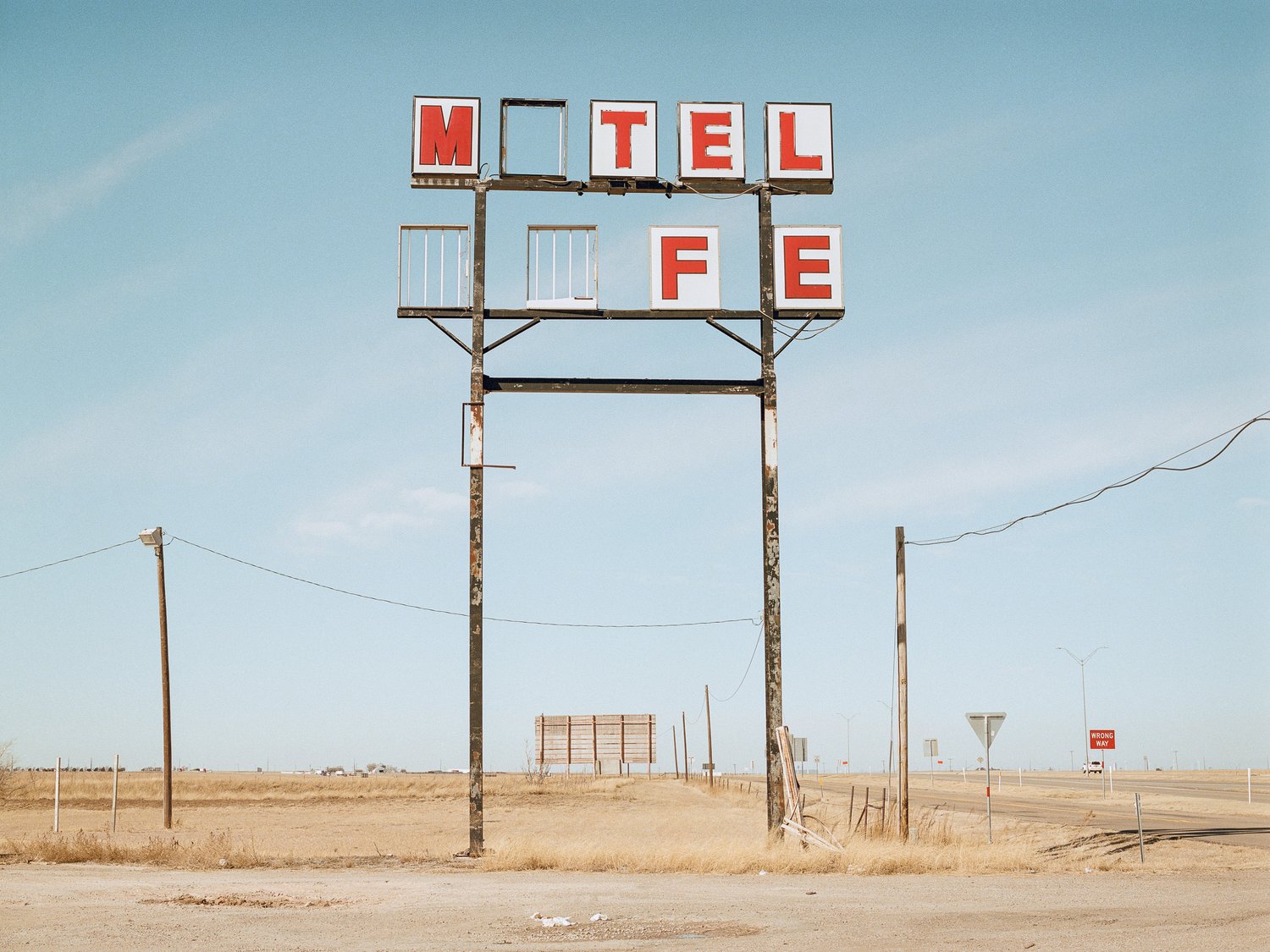 Photograph of a sign with damaged lettering in a desolate desert scene.