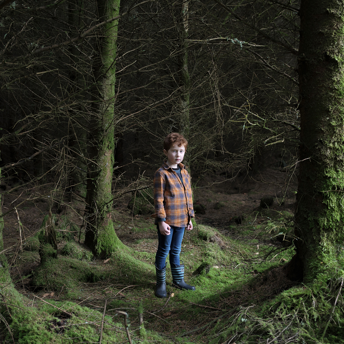A photograph of a young person stood in woods in the dark.