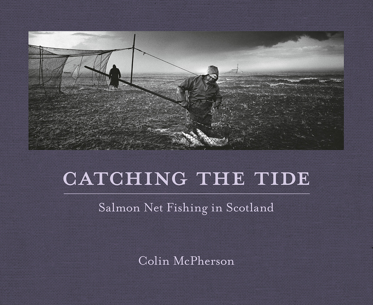 Photographers image of two fishermen working in the rain. Both are stood in the water. One holds a net containing a number of large fish.