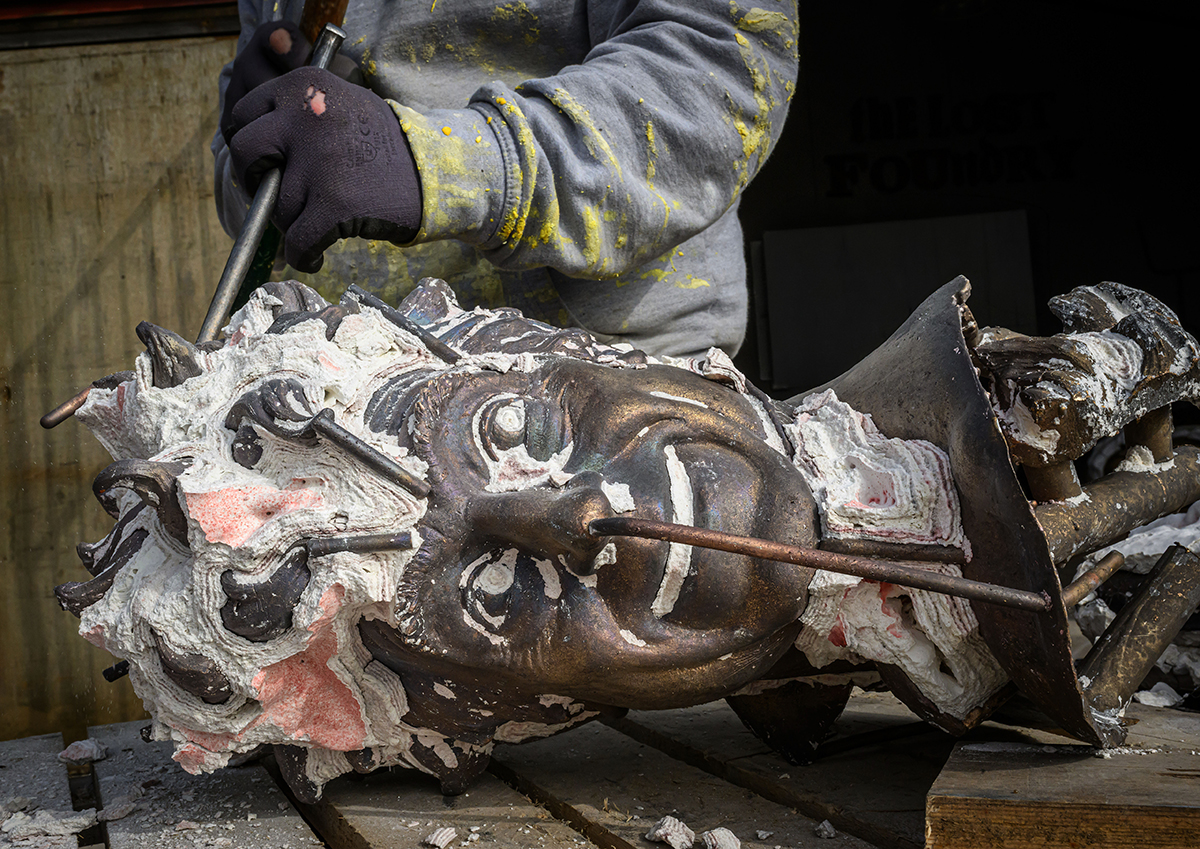 Sculptor chipping away material from a metal head.