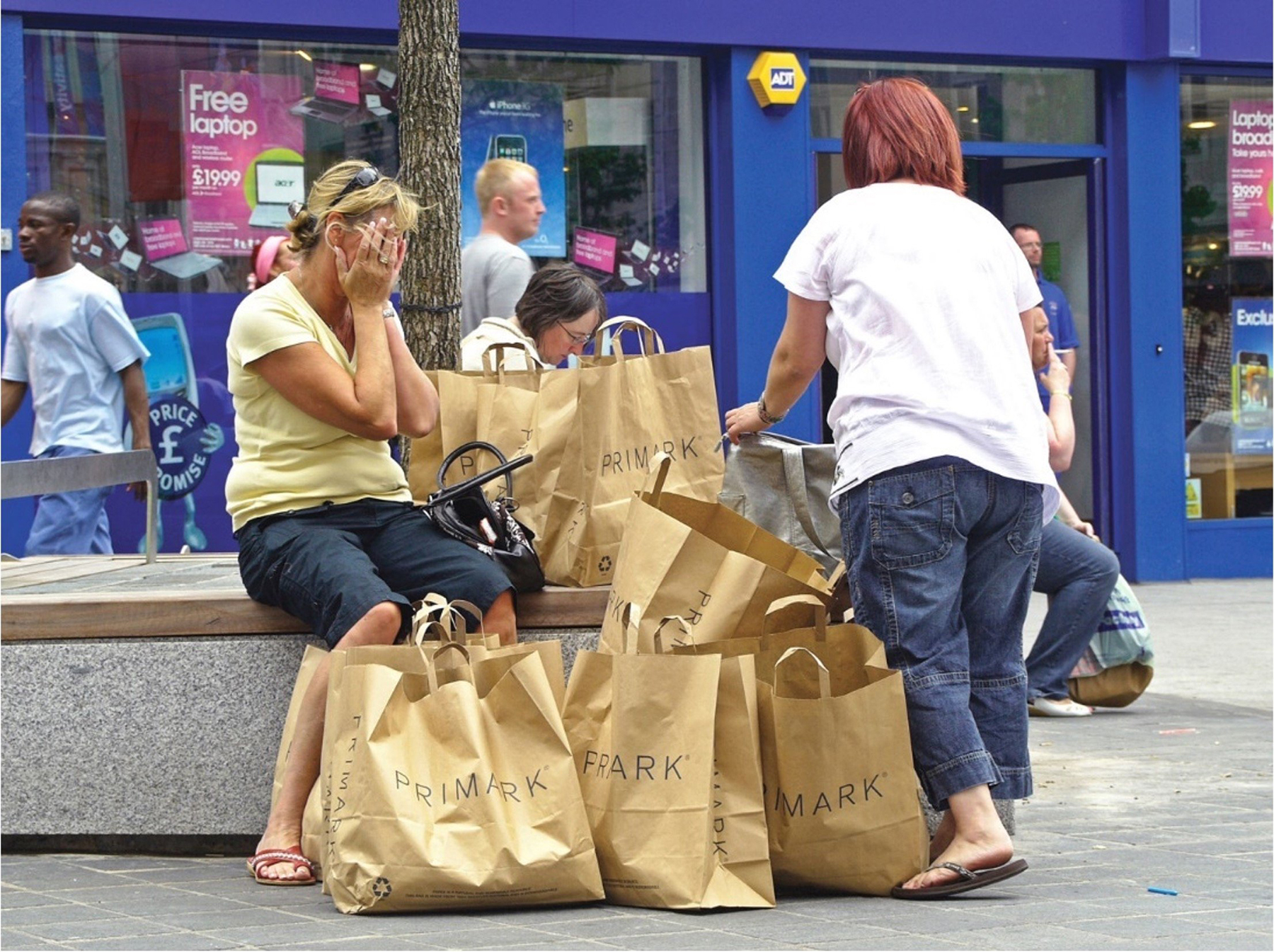 Photograph of highstreet scene with to women surrounded by shopping bags.